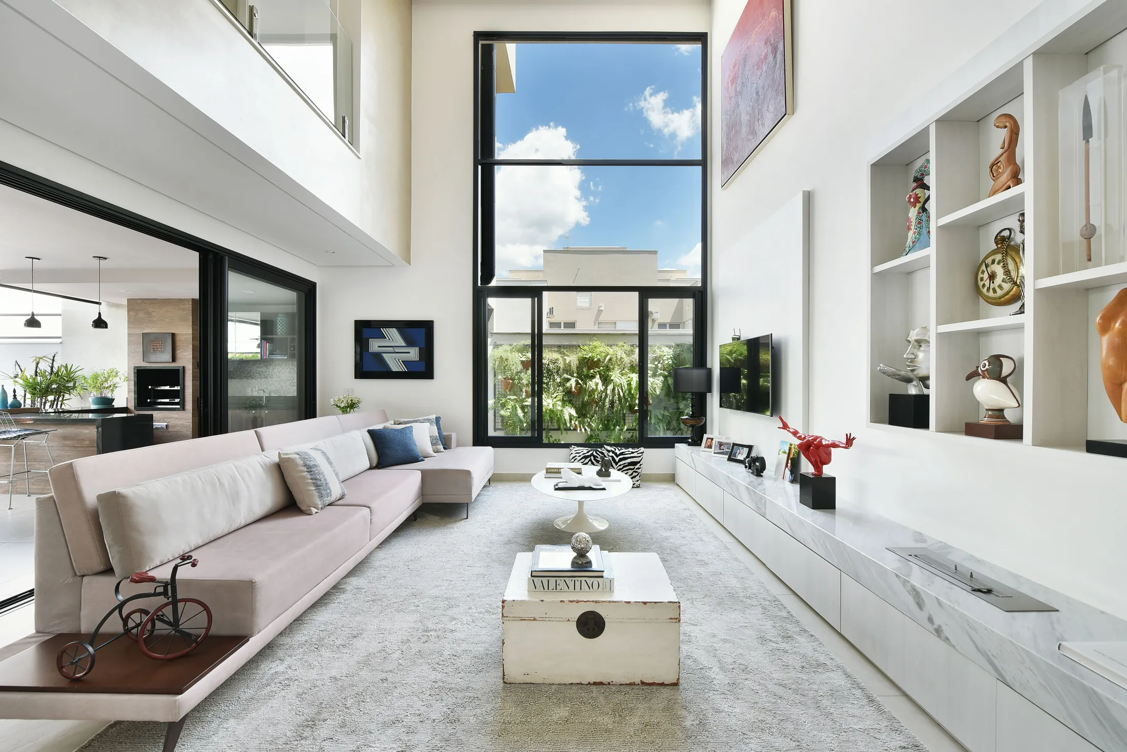 Sala de estar de pé-direito duplo, com sofá longo, janela alta e vista para o jardim